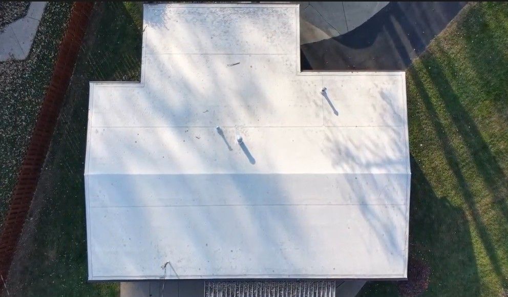 High-angle shot of a stadium roof, gray and white with equipment. A green field visible beyond the roof.