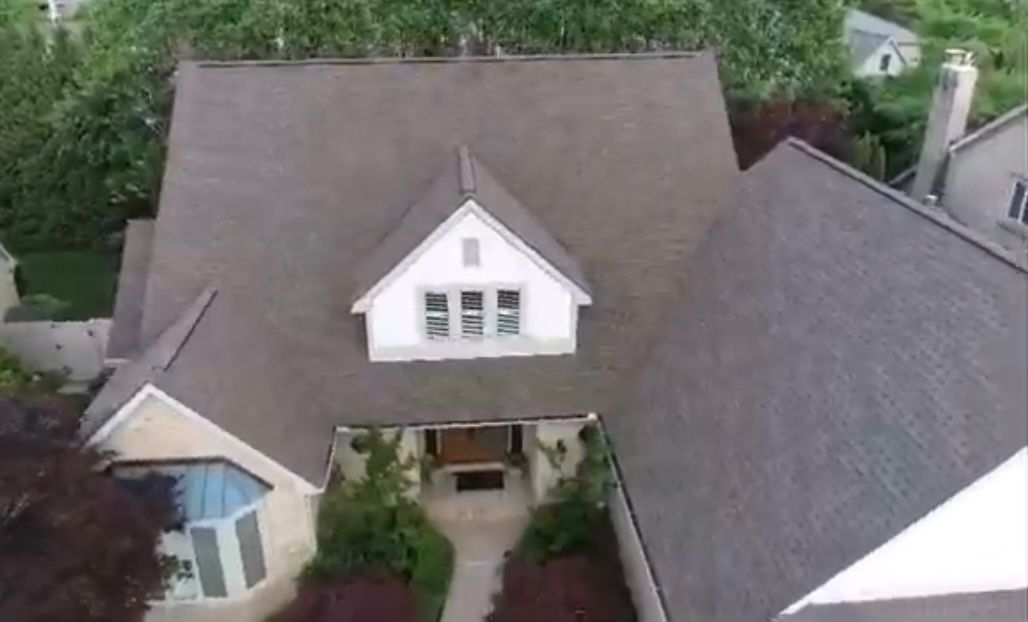 An aerial view of a large house with a brown roof surrounded by trees.