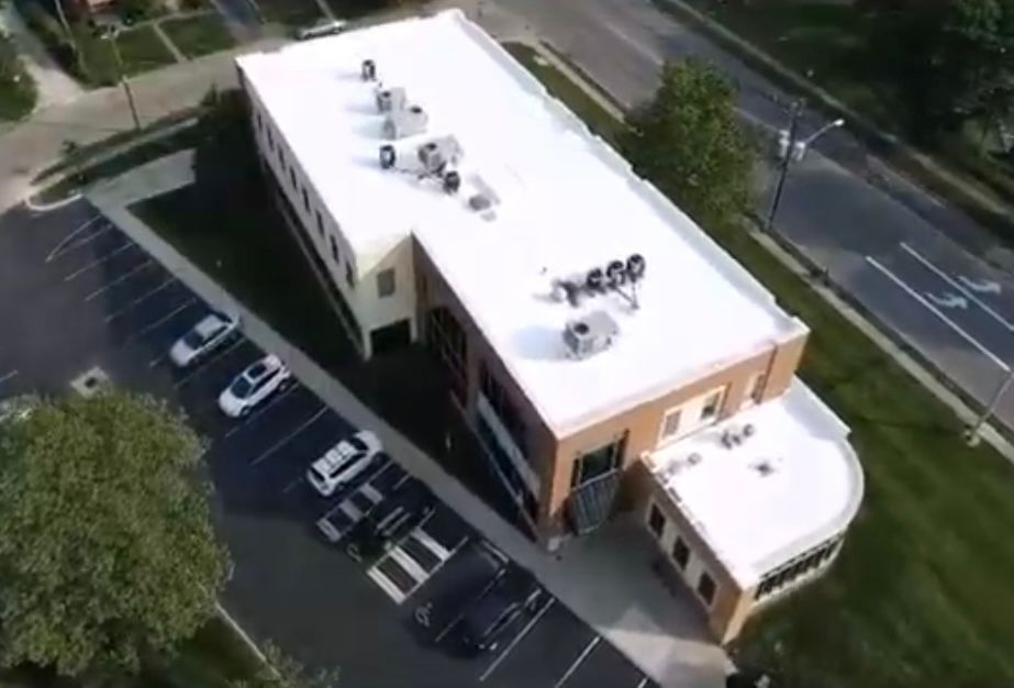 An aerial view of a building with a white roof and a parking lot.