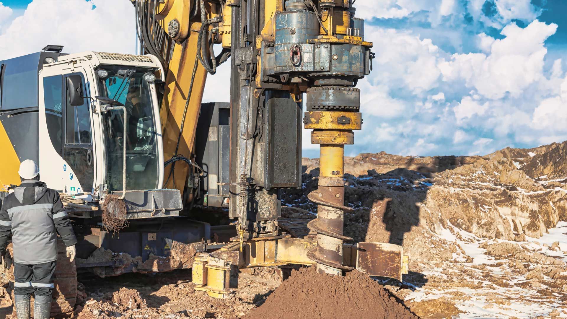 Large drilling machine operating at a construction site with soil piled beneath the auger.