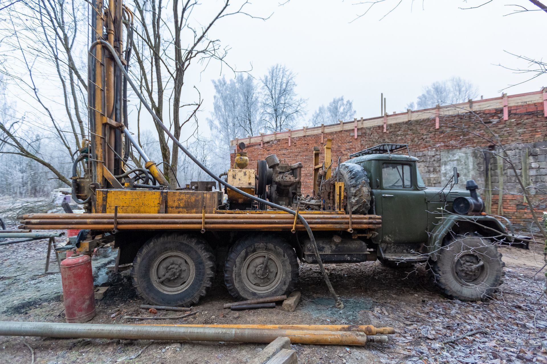 Drilling rig on a truck, outdoors near a brick wall, possibly for well water.