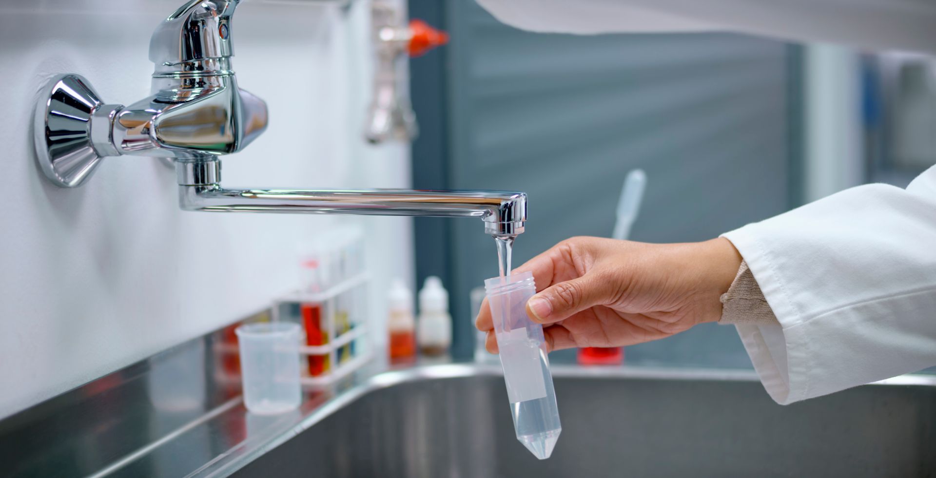 A person is holding a test tube in front of a sink.