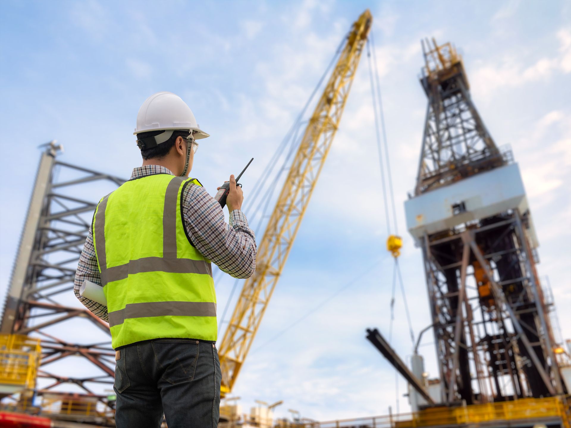 Well Drilling Contractor overseeing drilling rig and crane operations at construction site.