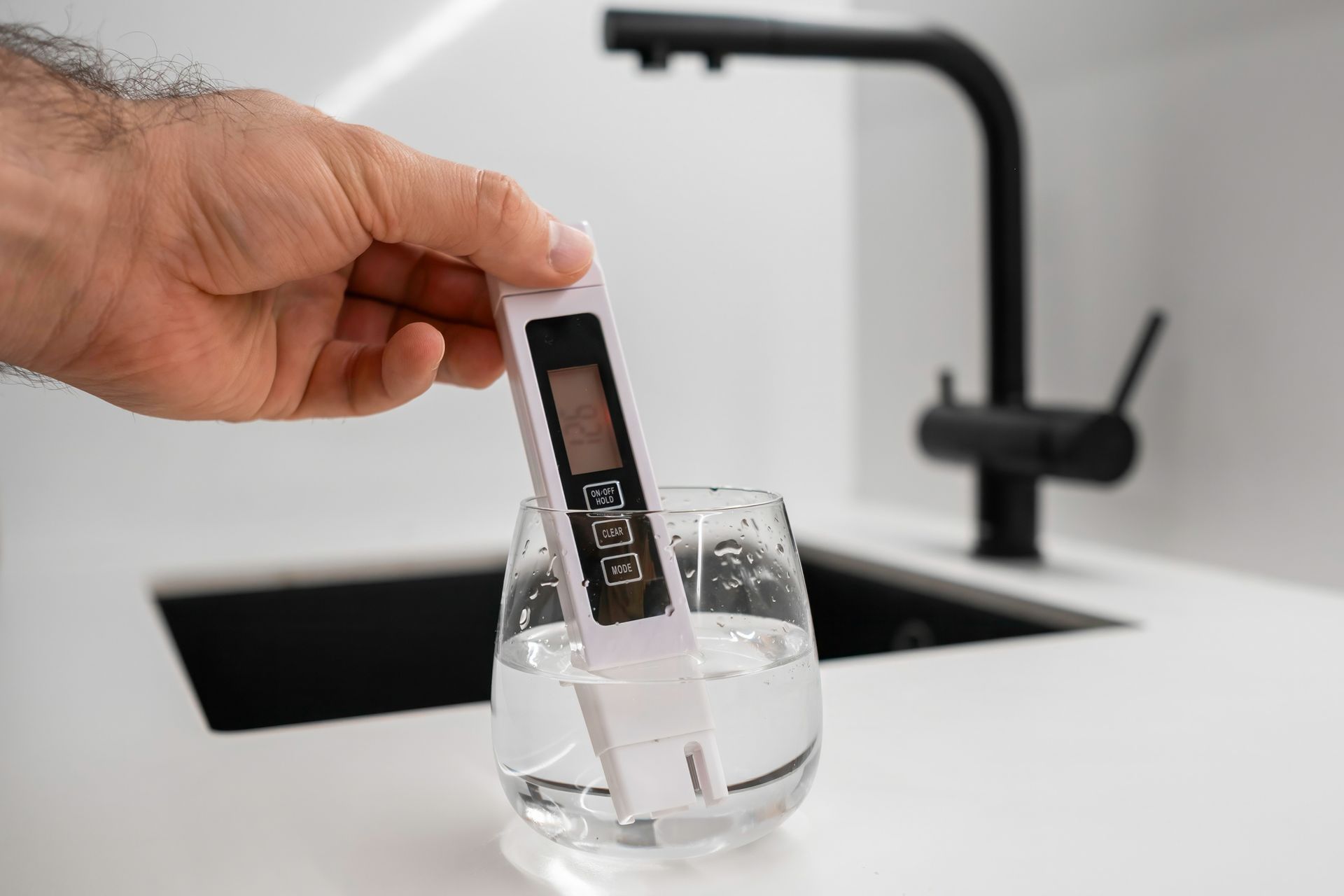 A person is holding a digital thermometer over a glass of water.