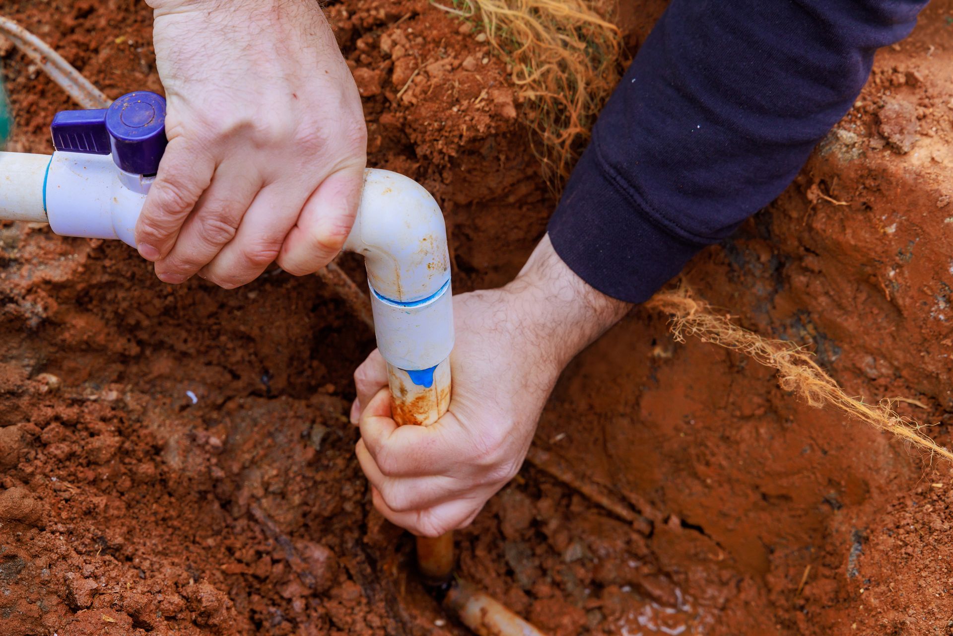 A person is fixing a pipe in the dirt.