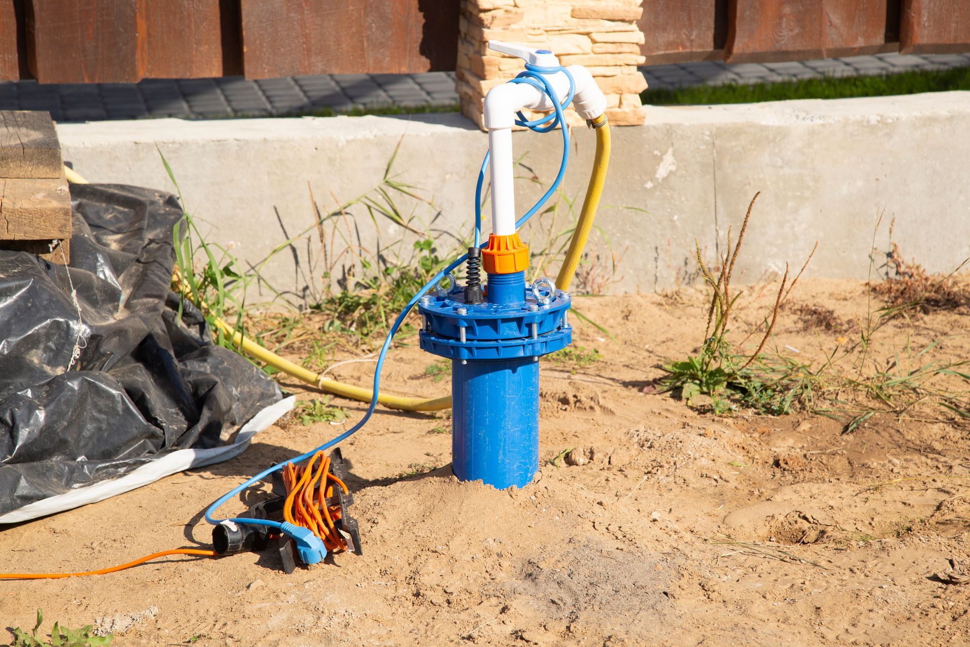 A water pump is sitting in the dirt next to a hose.