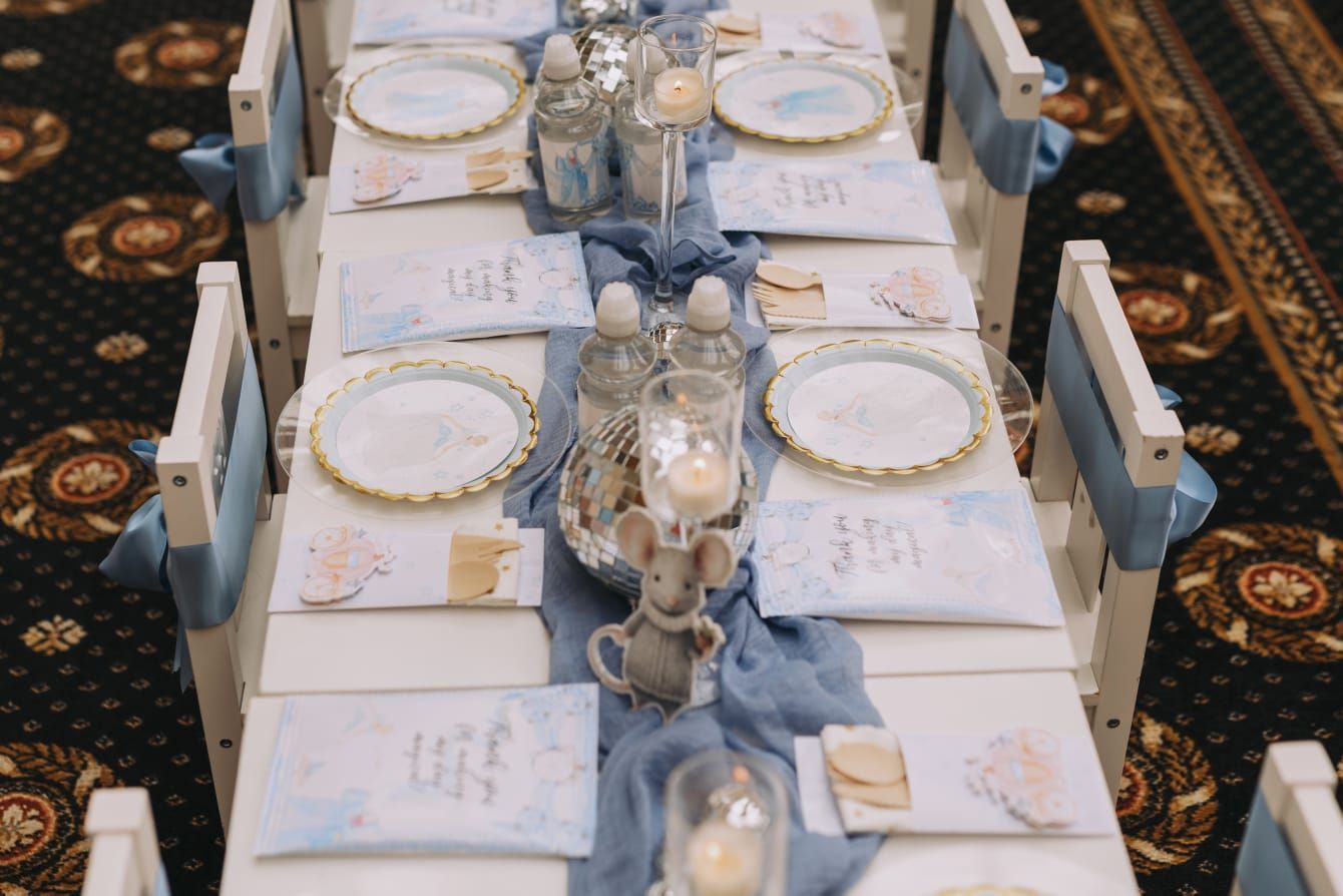 A long table with plates , napkins , candles and a mouse on it.