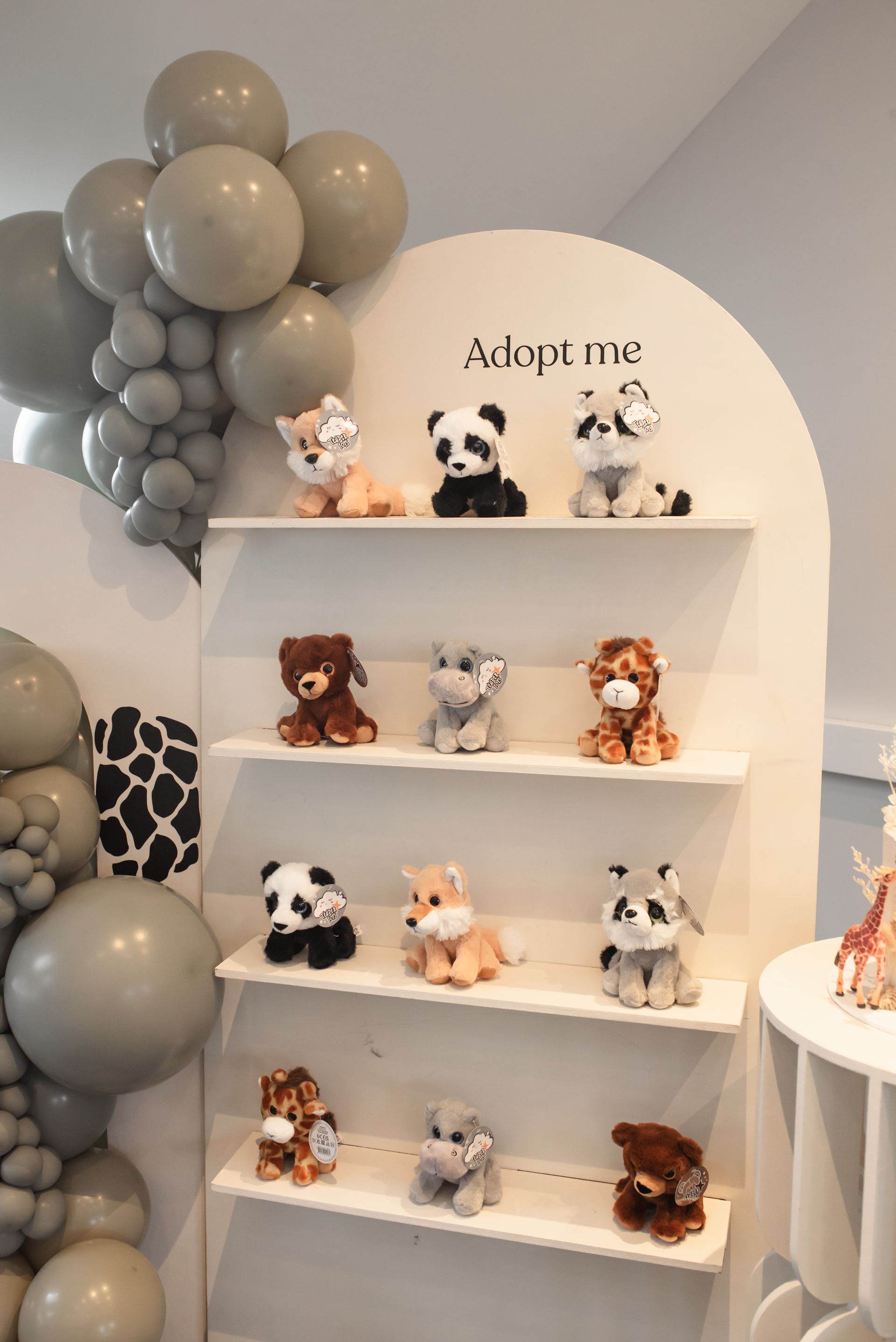 A display of stuffed animals on shelves with balloons in the background.