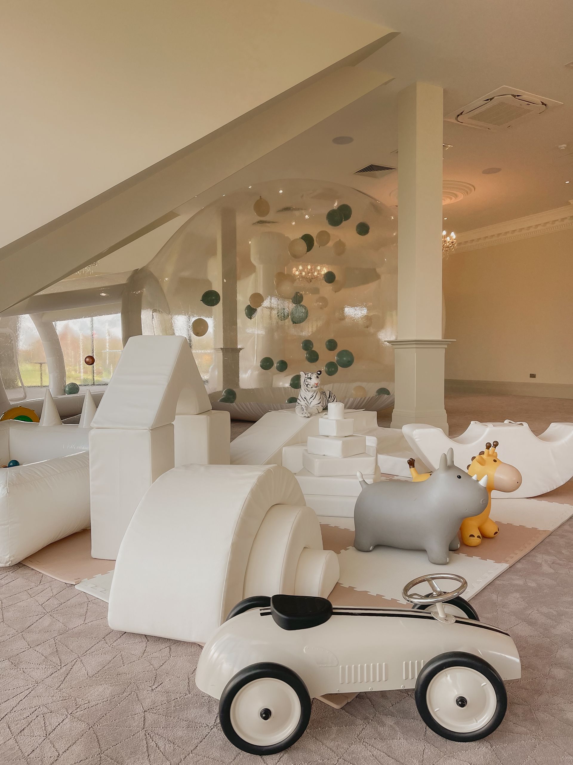 A white toy car is sitting on the floor in a room filled with toys.