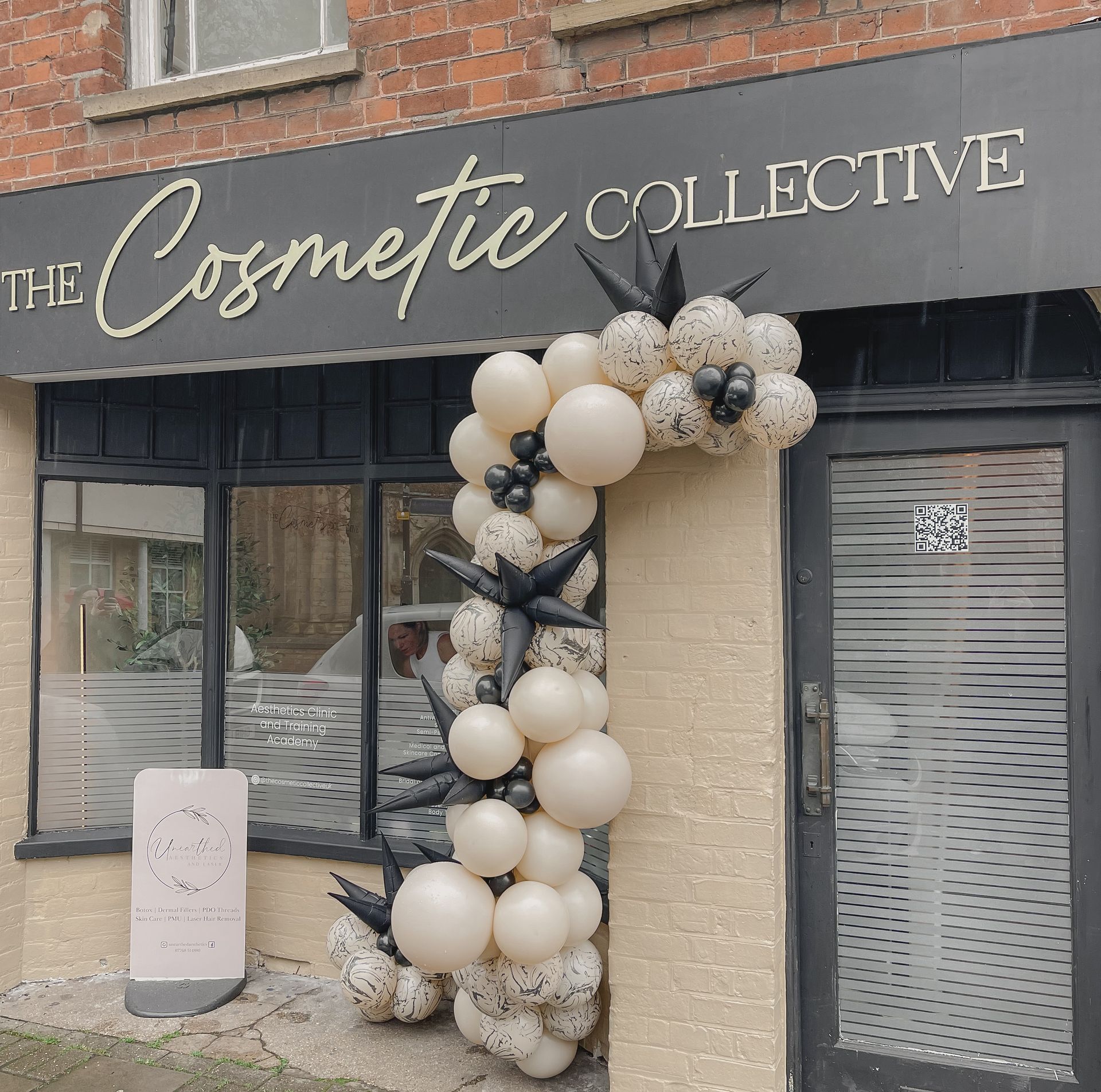 A store front with balloons and a sign that says the cosmetic collective