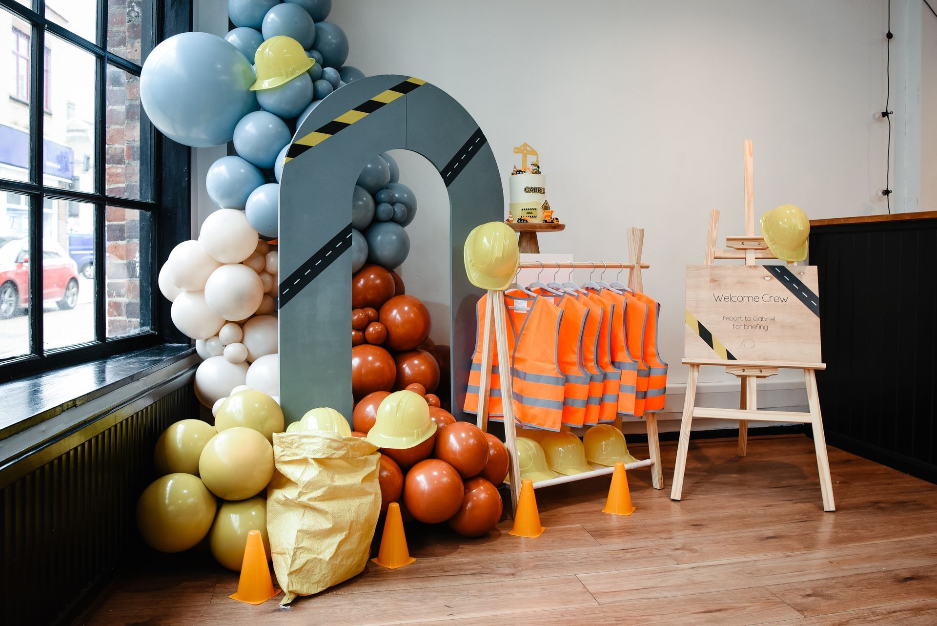A room decorated with balloons , hard hats , vests and cones.