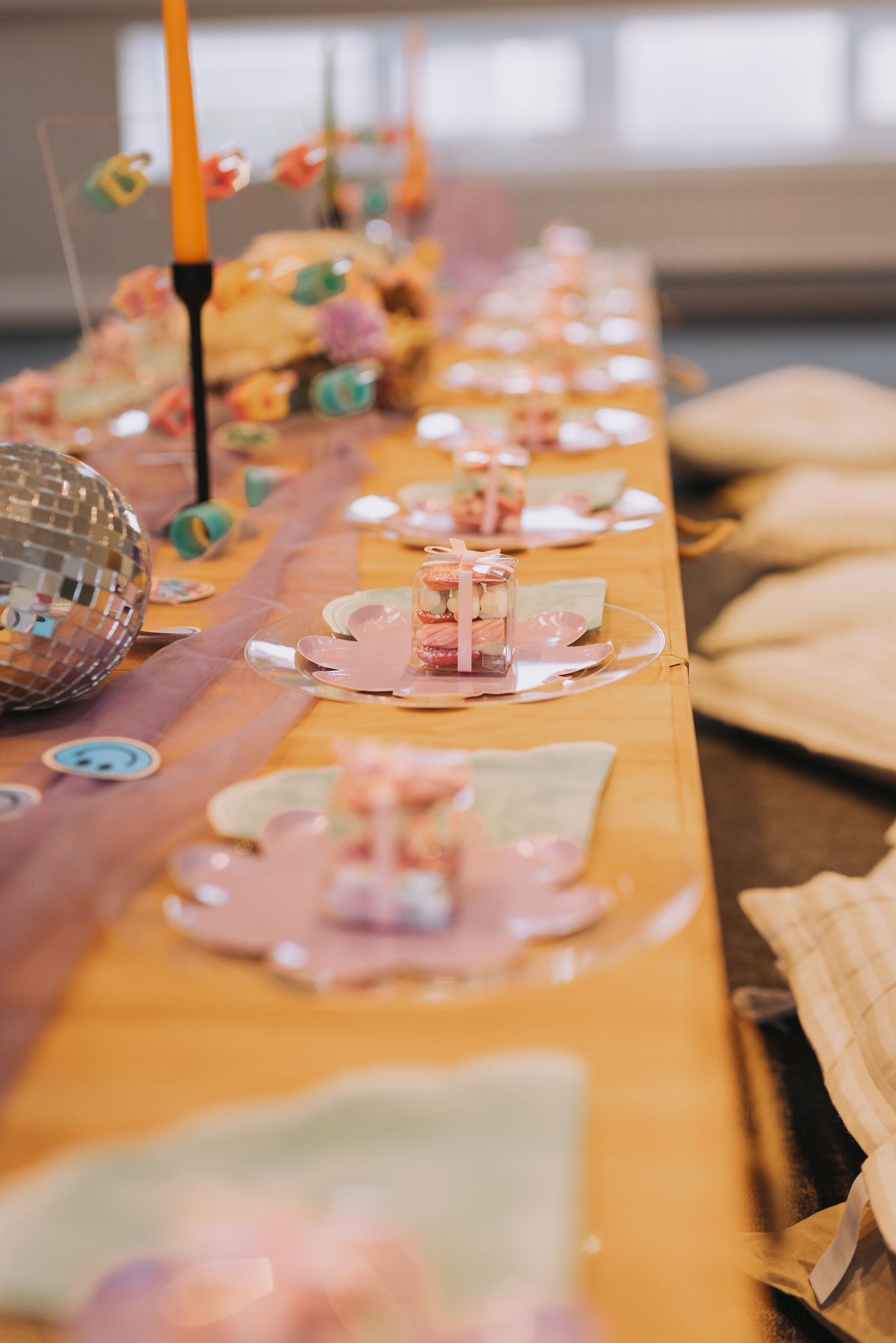 A long table with plates , napkins , candles and a disco ball on it.