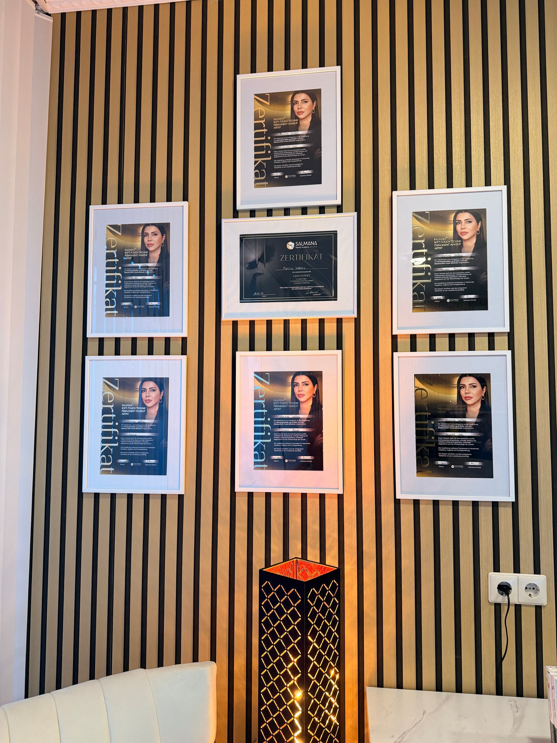 In einem gemütlichen Zimmer hängen gerahmte Fotos an einer gestreiften Wand über einer dekorativen Lampe.