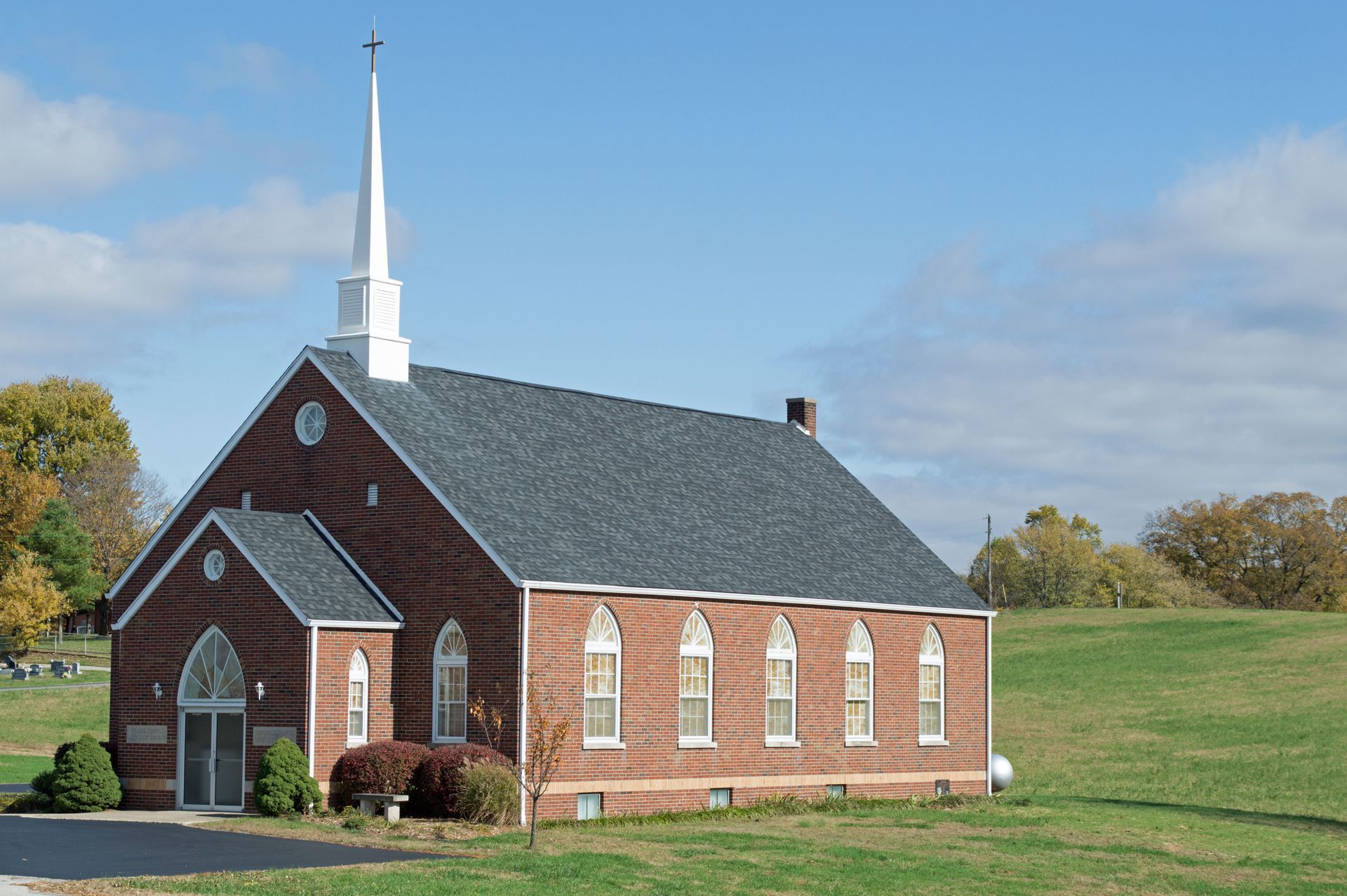 Small red brick church with white steeple in a grassy field under a blue sky