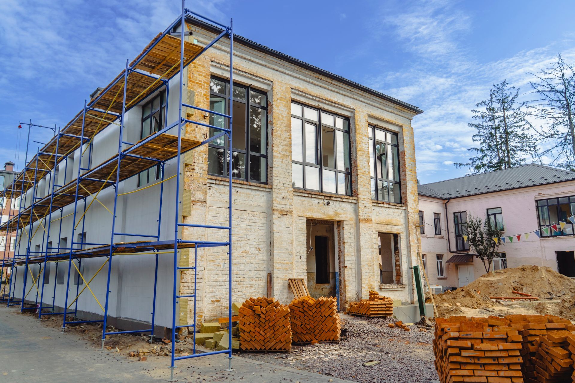 Two-story building under renovation with blue scaffolding and stacked bricks outside