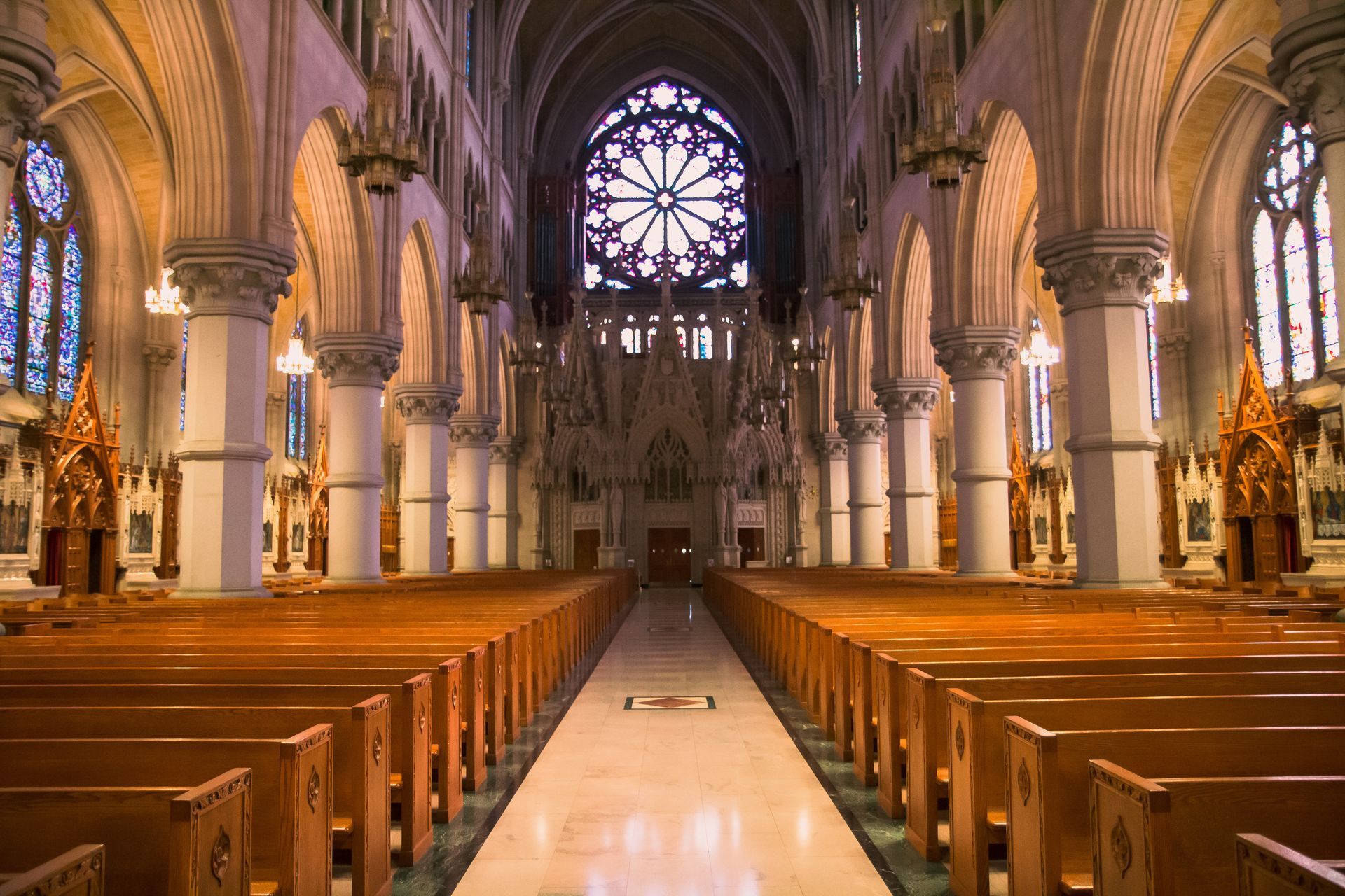 Interior of a grand cathedral with wooden pews, stone arches, and a stained-glass rose window.