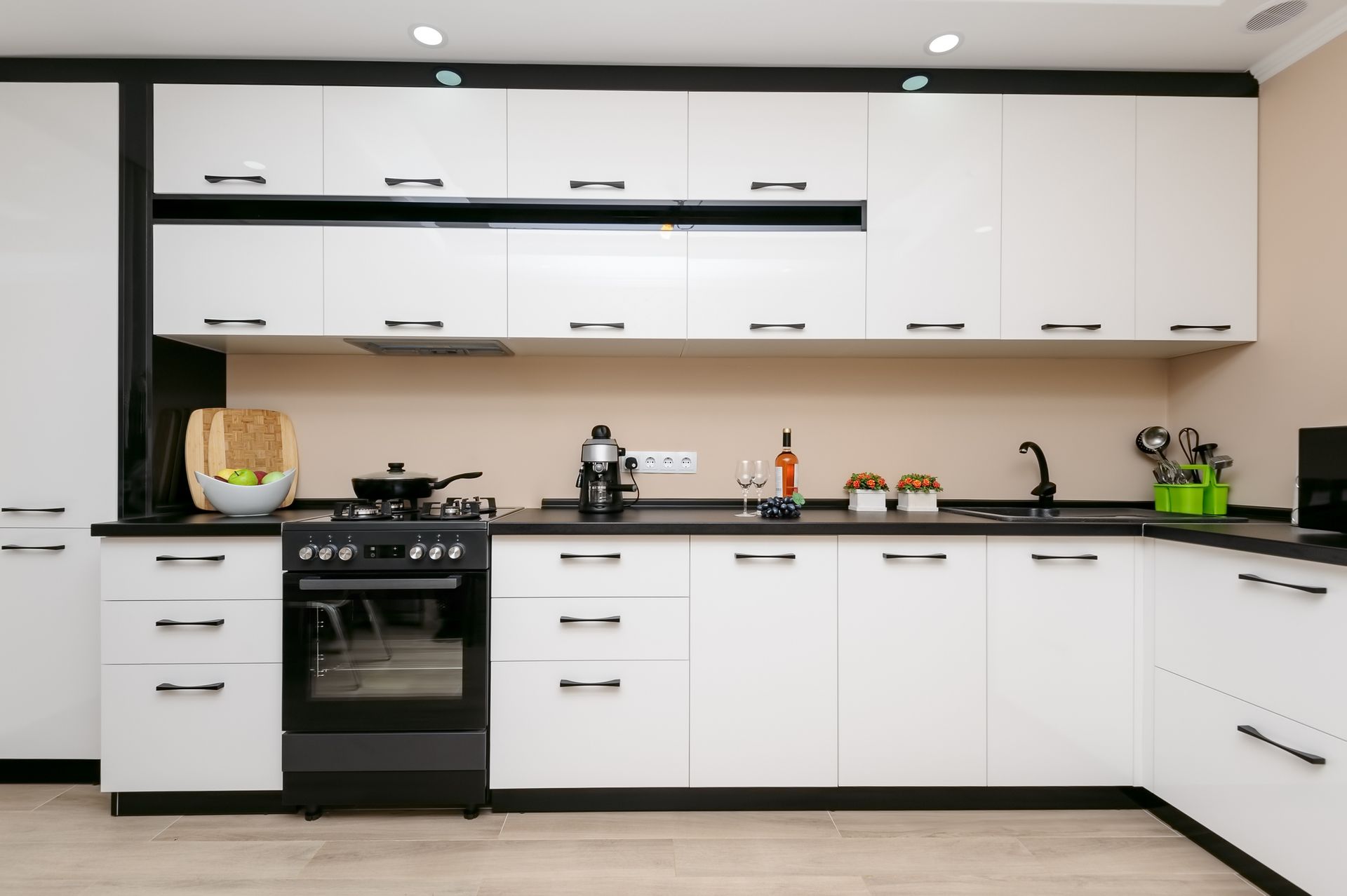 Modern white kitchen with black countertops, stove, sink, and cabinets לאורך the wall