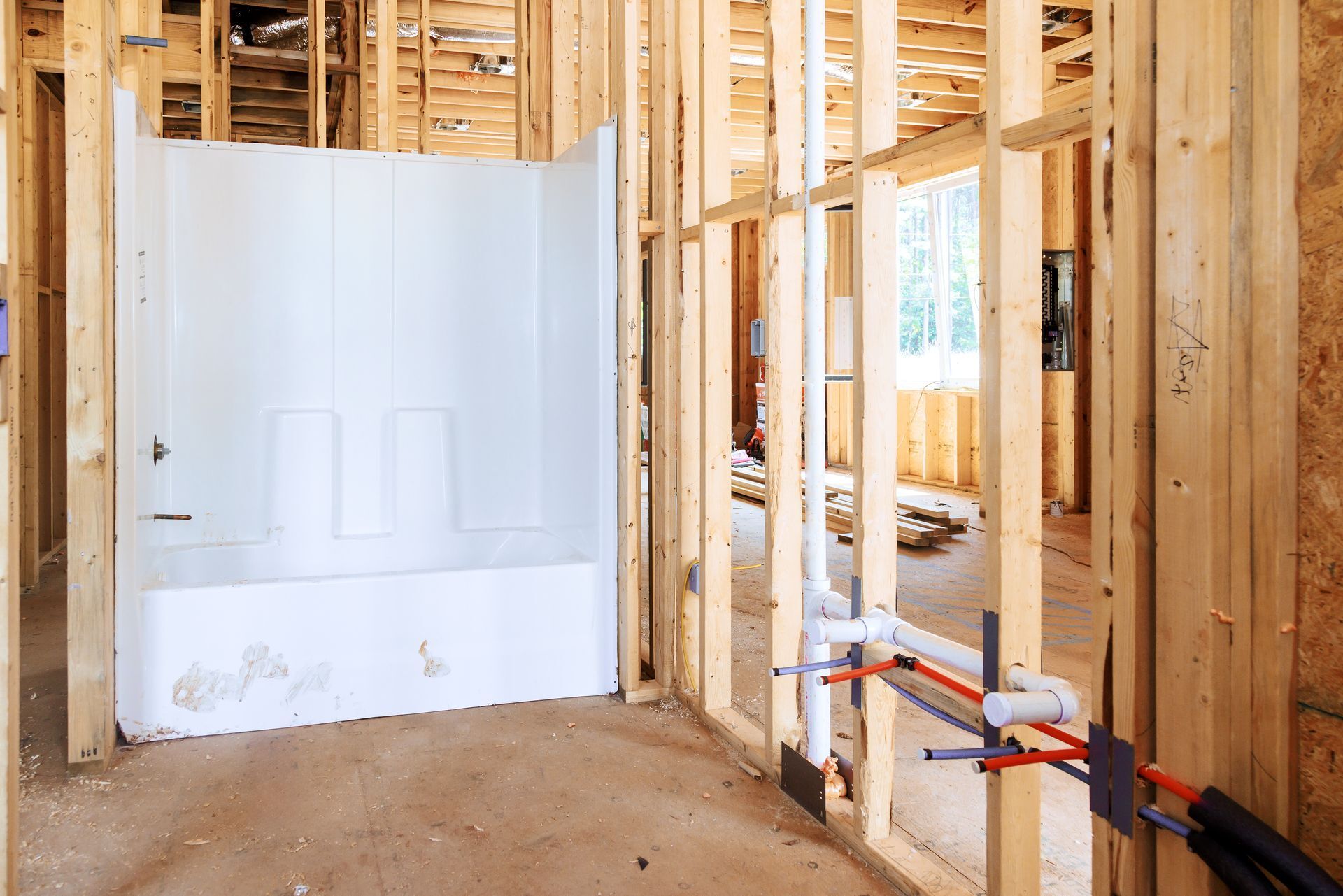 Partially built bathroom with white tub, exposed wooden framing, and plumbing during house construction