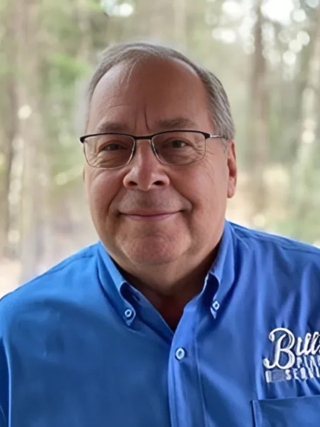 A man wearing glasses and a blue shirt is smiling for the camera.