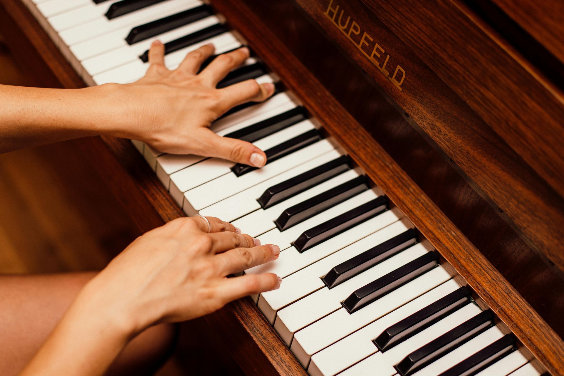 Hands playing a wooden piano, pressing the white and black keys. Close up shot.