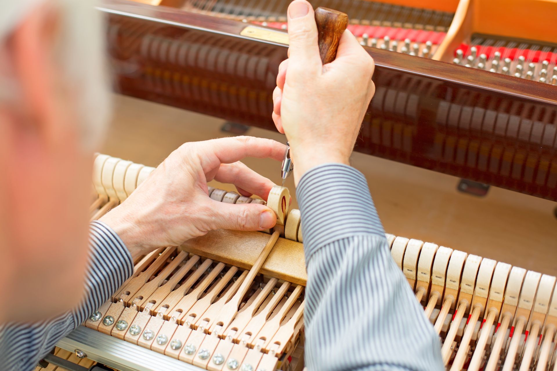 A man is working on a piano with a screwdriver.