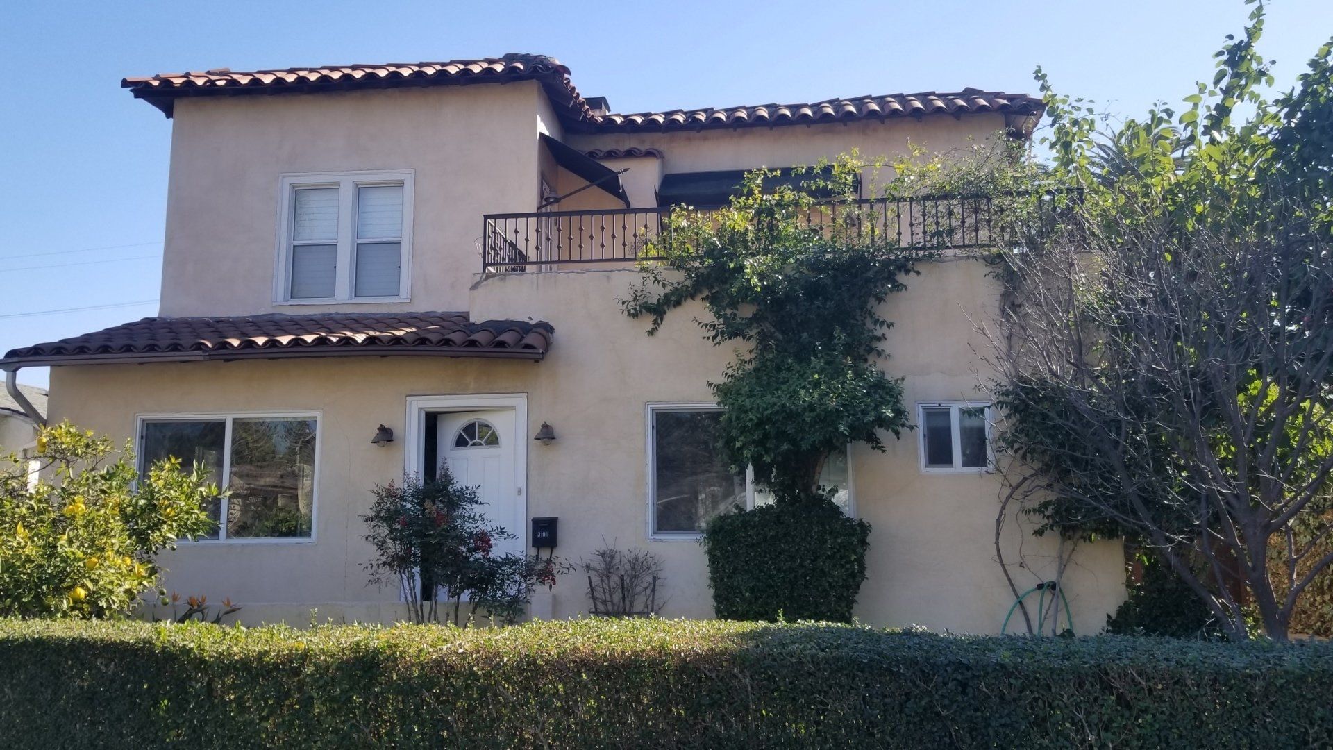 A house with a balcony and a hedge in front of it