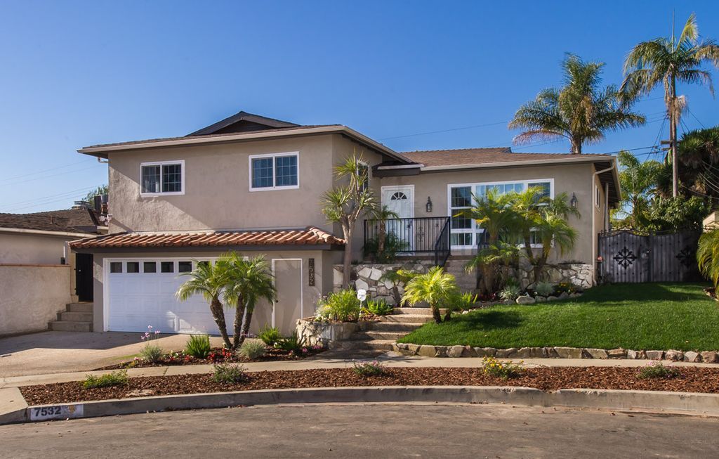 A large house with a white garage door is sitting on top of a lush green hillside.