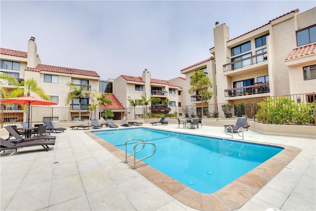 A large swimming pool surrounded by chairs and umbrellas in front of a building.