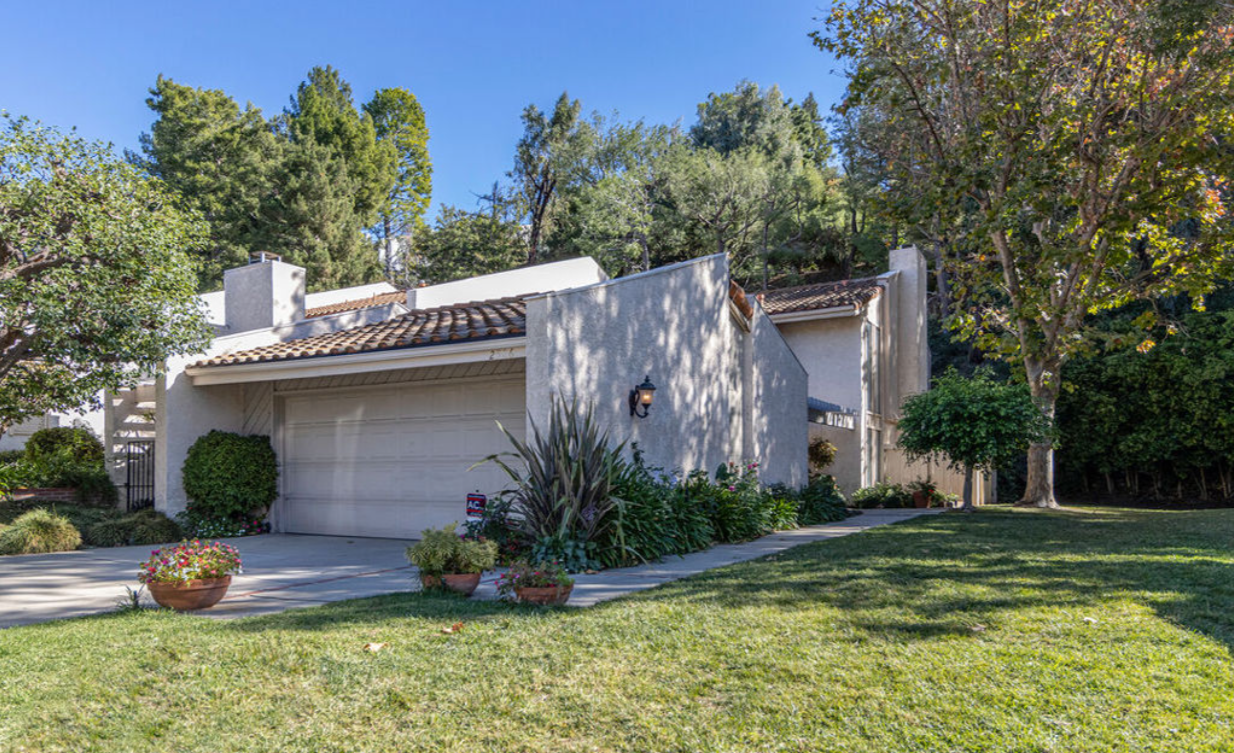 A white house with a garage and a lush green lawn in front of it.
