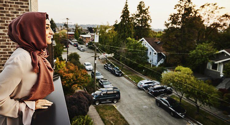 A woman in a hijab is standing on a balcony overlooking a city street.