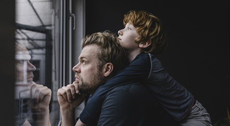 A man and a boy are looking out of a window.