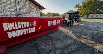 A red dumpster is parked in front of a brick building.