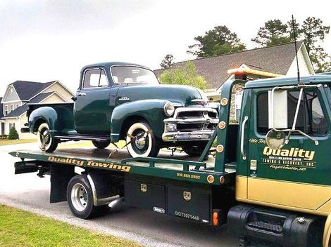 an old green truck is being towed by a quality tow truck