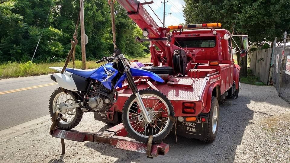 a red tow truck is towing a dirt bike on a trailer .