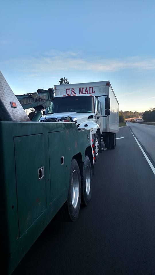 a tow truck is towing a us mail truck on the side of the road .