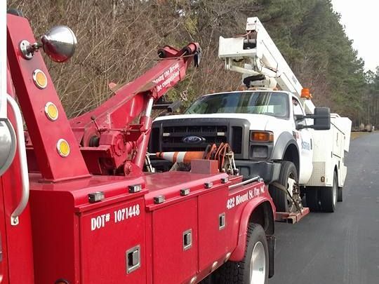 a red tow truck is towing a white truck on the side of the road .