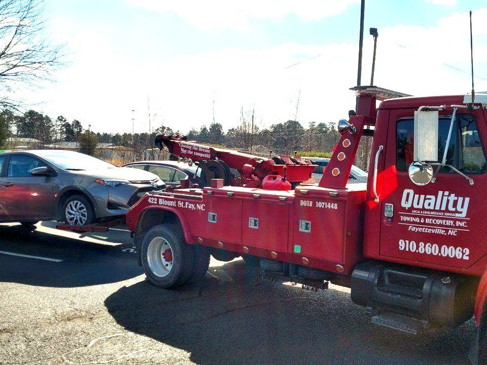 a quality tow truck is towing a car in a parking lot