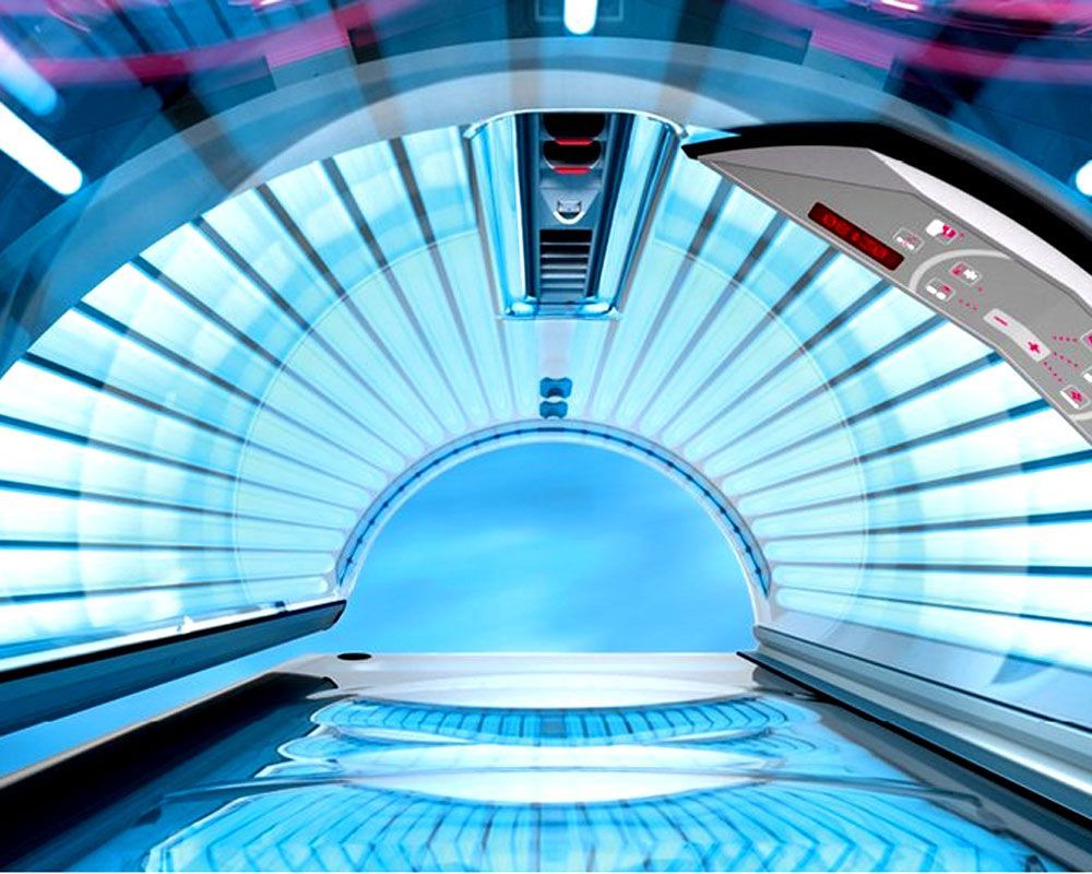 Innenansicht eines Solariums, das blaues Licht ausstrahlt. Gewölbter Innenraum, Bedienfeld auf der rechten Seite.