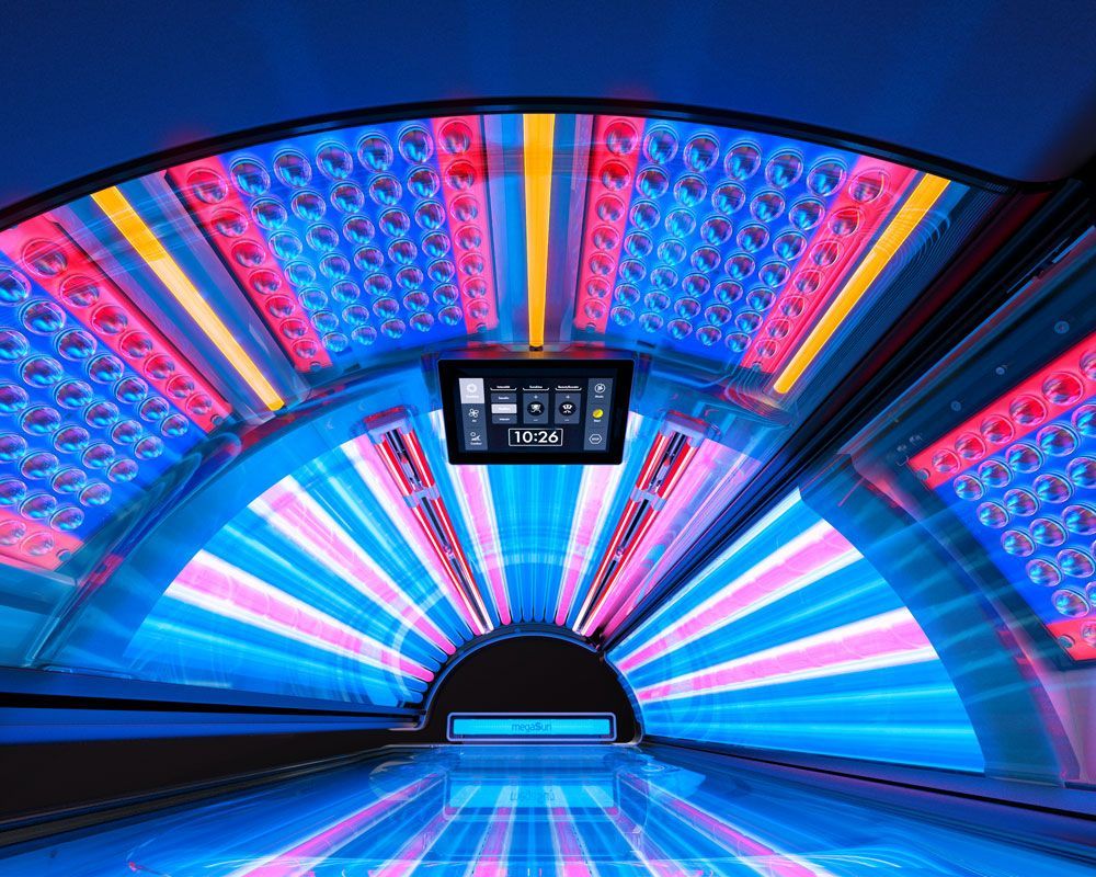 Innenansicht eines Solariums mit blauen, rosa und roten Lichtern. Bedienfeld sichtbar.
