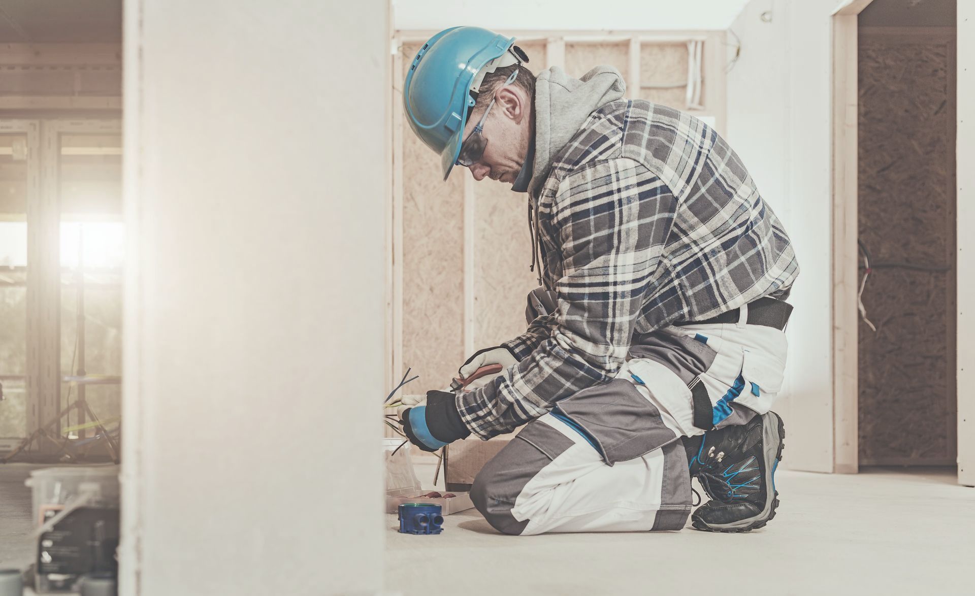 A man is kneeling down in a room while working on a wall.