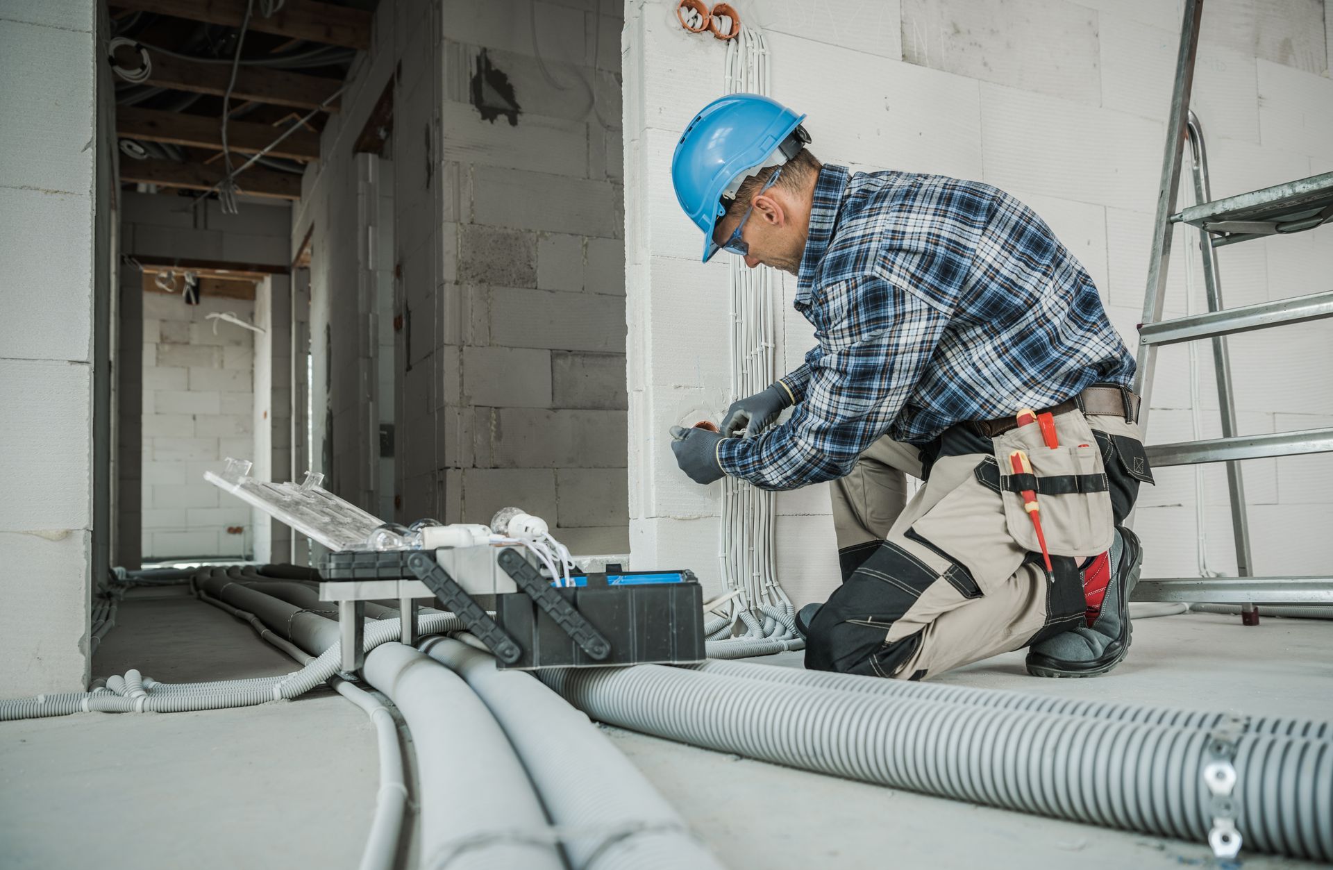 A man is kneeling down in a room while working on electrical wires.