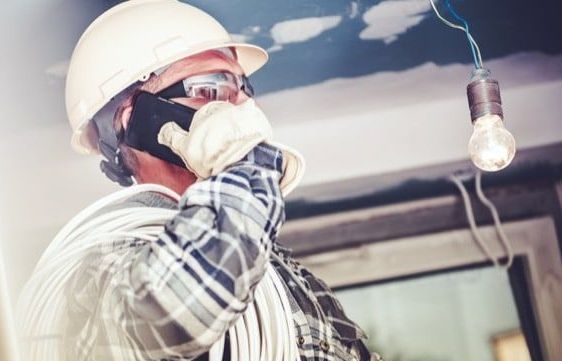 A man is talking on a cell phone while looking at a light bulb hanging from the ceiling.