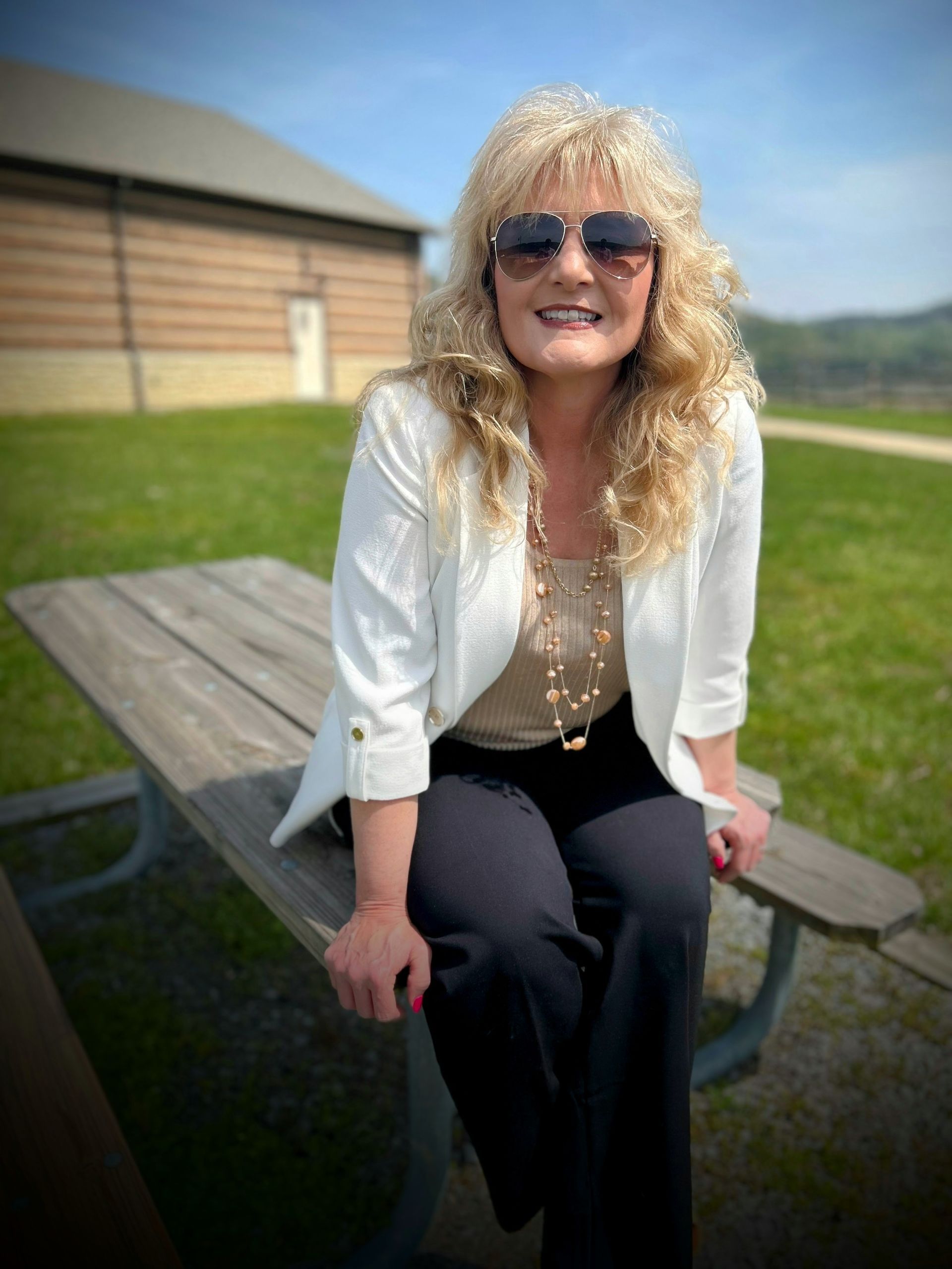 A woman wearing sunglasses is sitting on a picnic table.