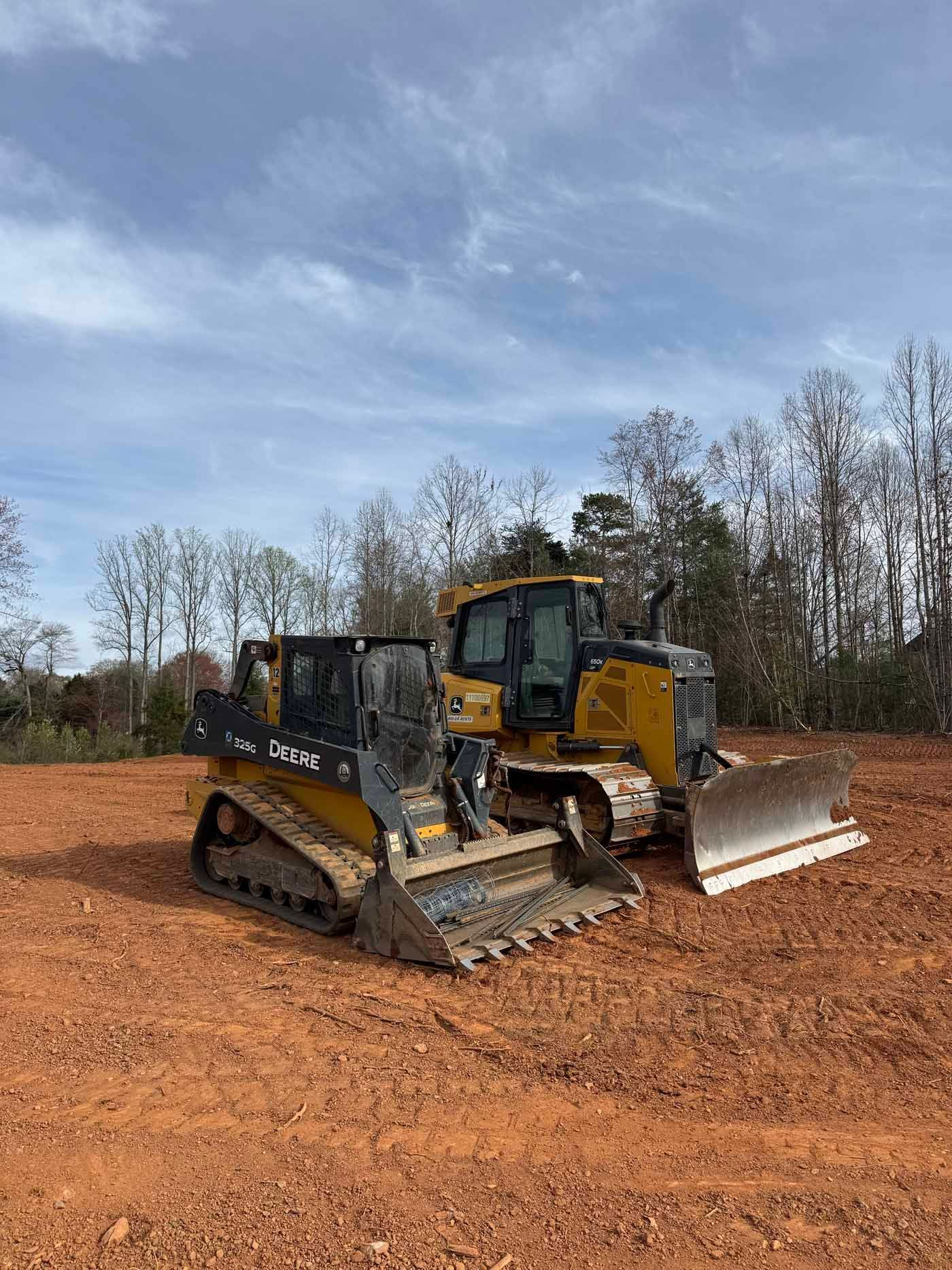 Two bulldozers are parked in a dirt field.