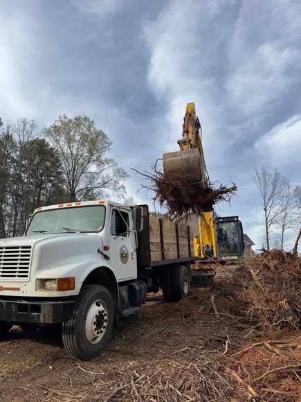 A white truck is sitting in a pile of wood chips next to a yellow excavator.