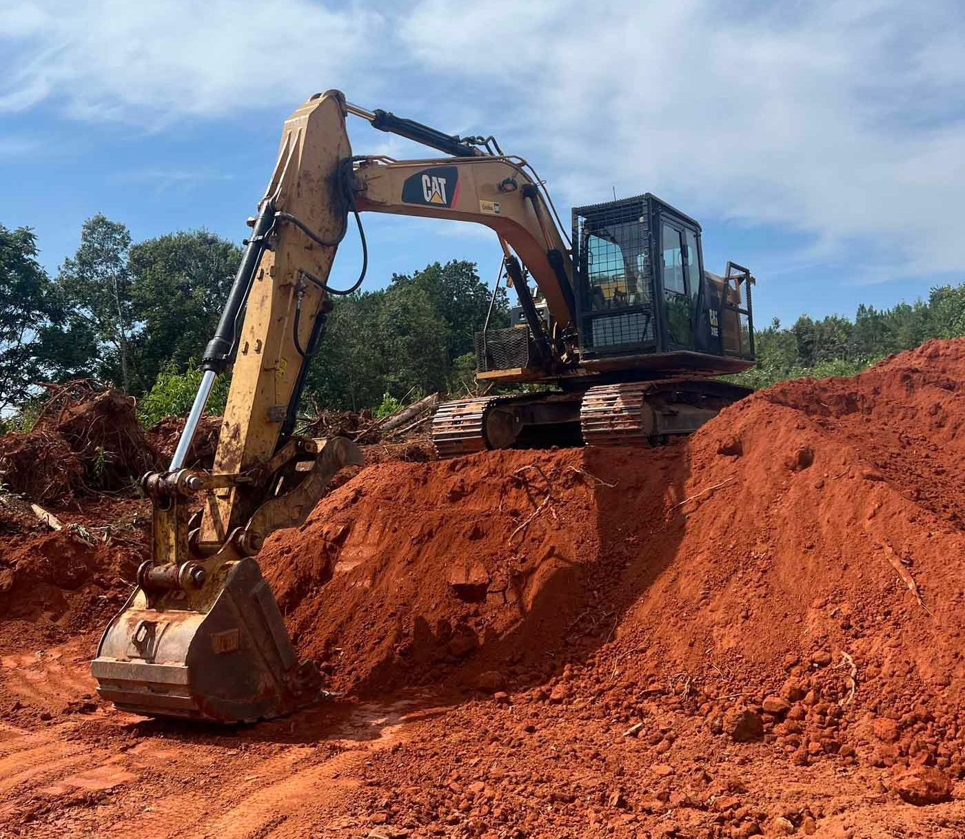 A cat excavator is digging in a pile of dirt.