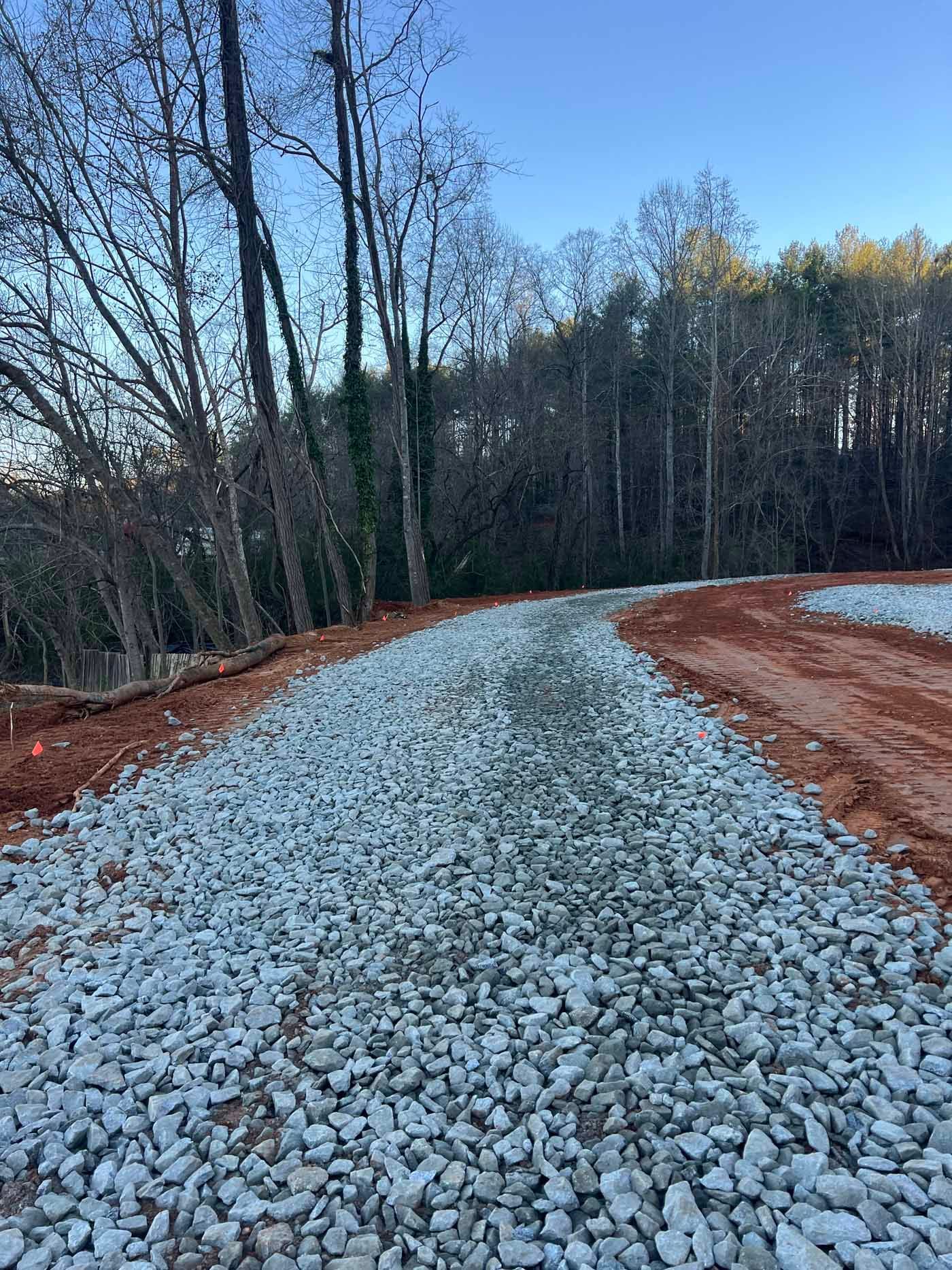 A gravel road going through a forest with trees in the background.