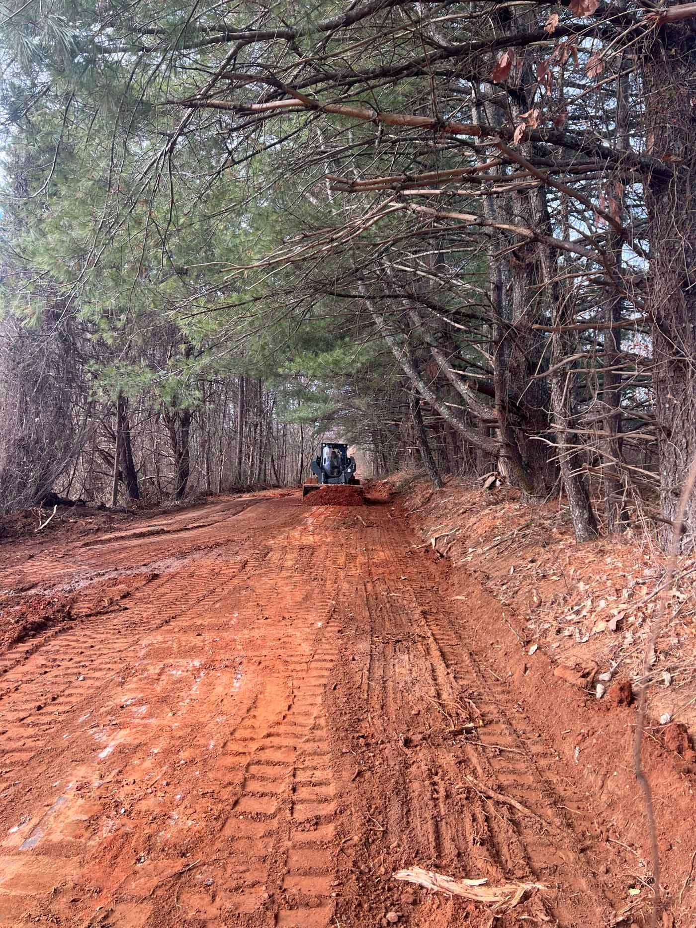 A tractor is driving down a dirt road in the woods.