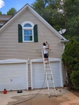 A man is standing on a ladder washing the side of a house.