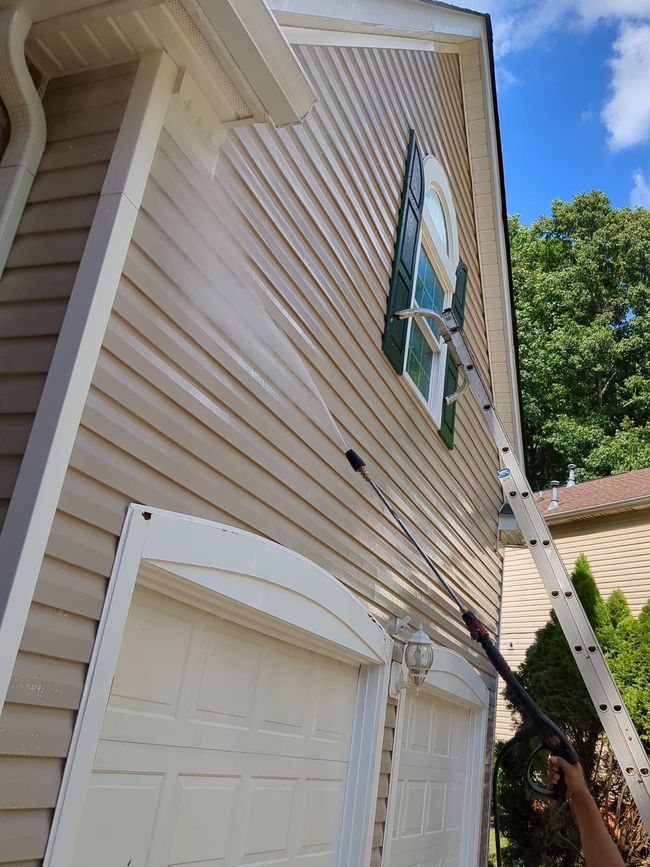 A person is painting the side of a house with a sprayer.